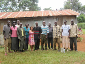 An IHN representative posing with a group of locals outside a metal roofed structure