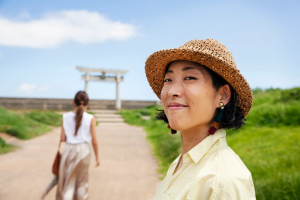 Japanese stands on a green scenery with a Japanese gate and looks into the camera