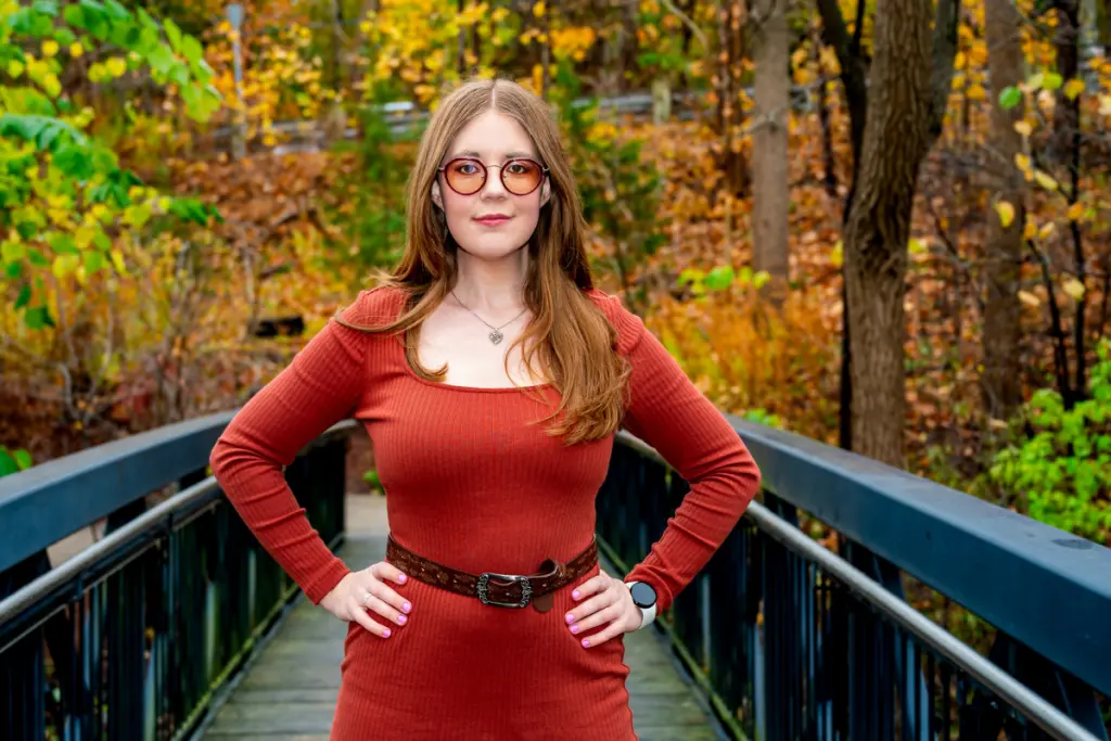 Lyndsay Fraser standing on a bridge surrounded by colorful autumn foliage in a wooded park.
