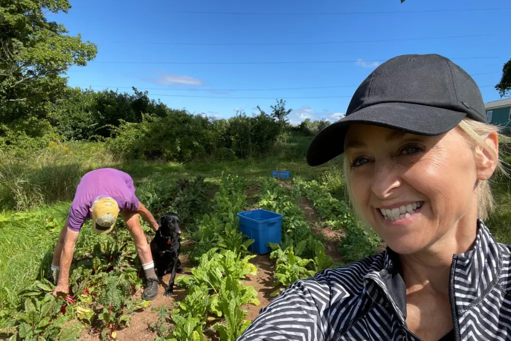 Lynn Swanson harvesting vegetables in a community garden alongside a fellow volunteer and a dog.