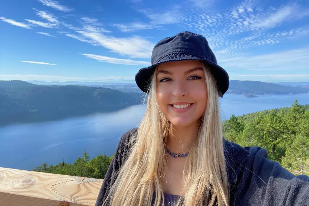 MacKenzie MacDougall smiling at a scenic mountain viewpoint overlooking a lake and forest.