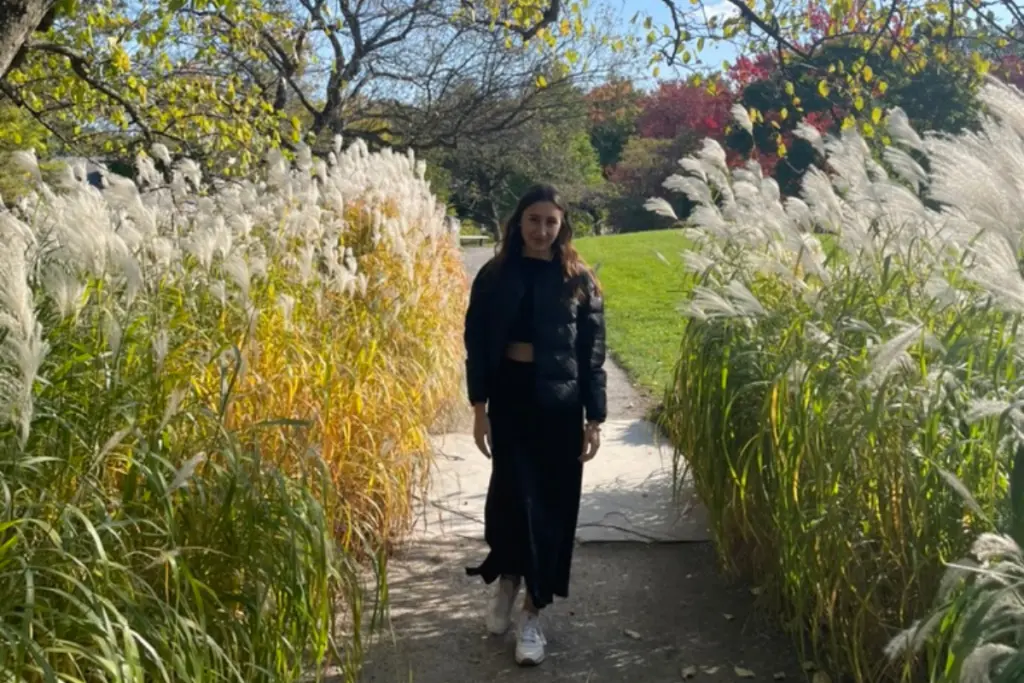 Rebecca Haywood walking through a garden pathway surrounded by tall ornamental grasses and autumn foliage.