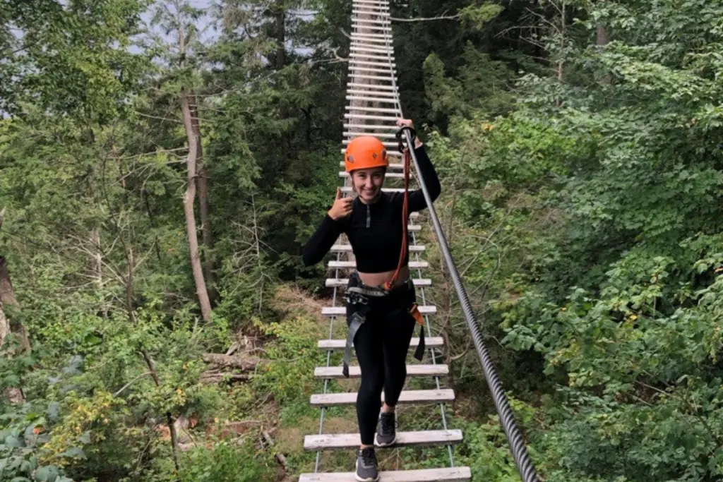 Rebecca Haywood crossing a suspended rope bridge during an outdoor forest adventure course.