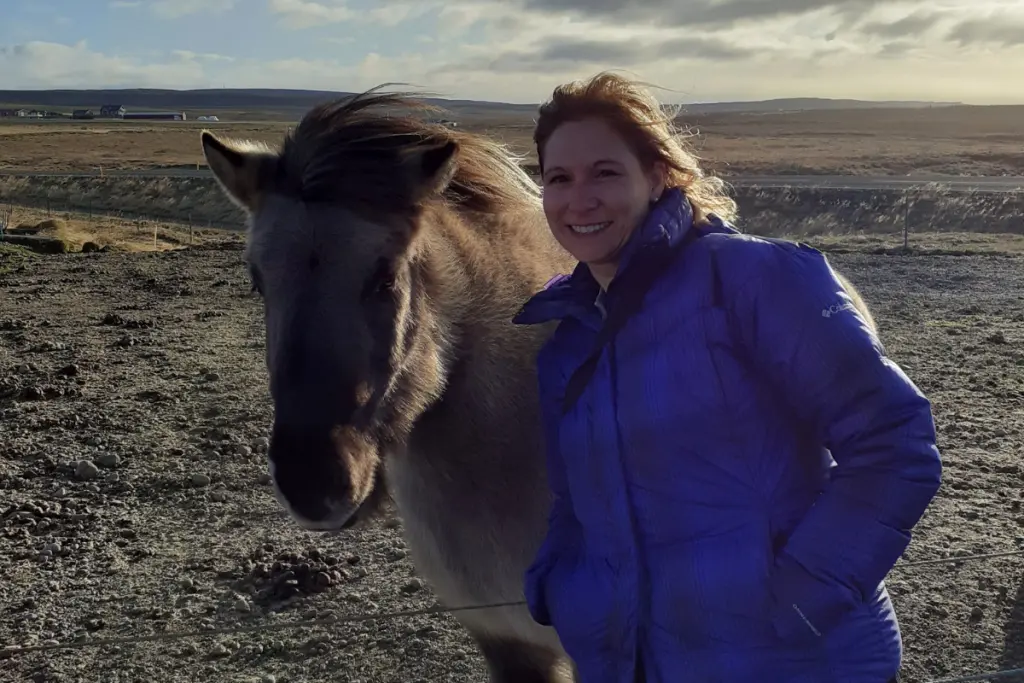Rebecca Haywood standing beside an Icelandic horse in a rural landscape.