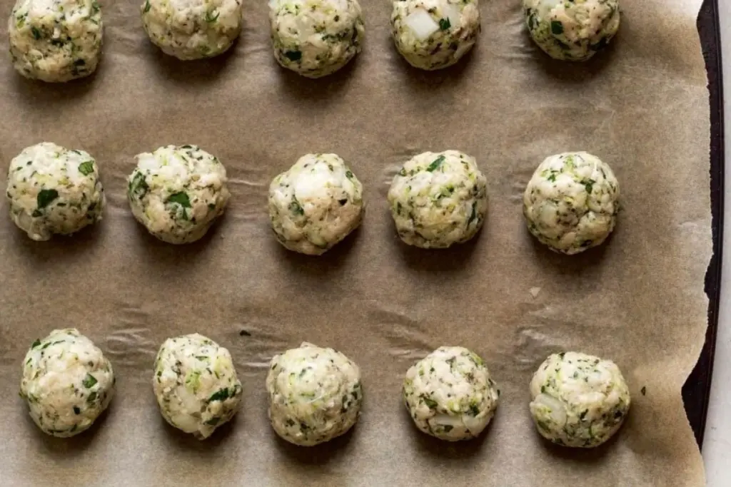 Homemade herb and vegetable fritters arranged on a baking tray before cooking.