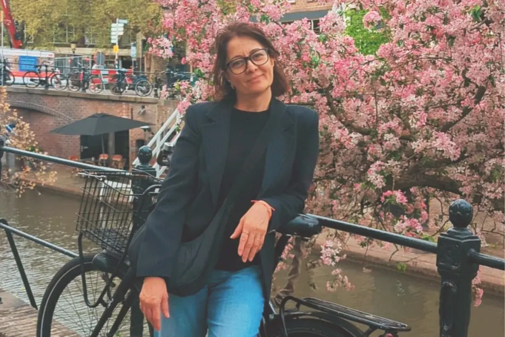 Viosa Koronica Barileva standing beside a canal lined with blooming cherry blossom trees during spring.
