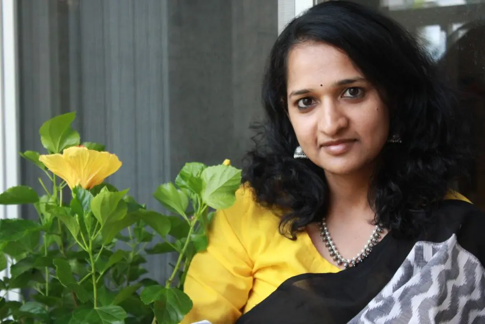 Anupama Kakarala posing beside a blooming yellow hibiscus plant, highlighting her connection with gardening and nature.
