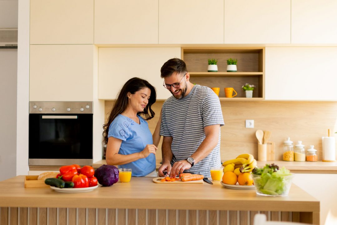 A couple joyfully prepares a meal in their stylish kitchen, surrounded by vibrant fruits and vegetables, filled with love and togetherness.
